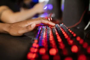 Manos de un jugador sosteniendo un control frente a una pantalla, con varios dispositivos gaming visibles