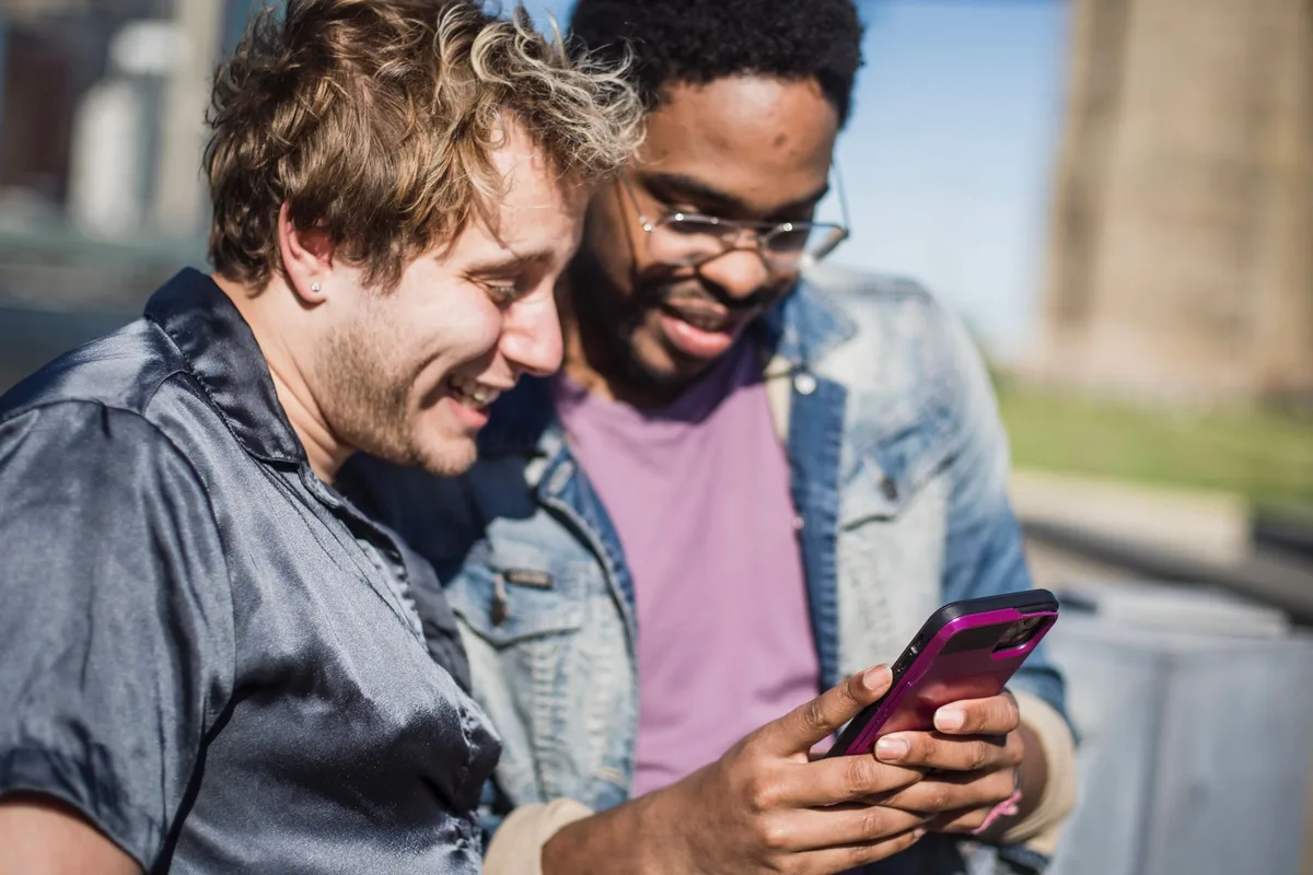 A group of friends reviewing shared expenses on an iPhone screen, hands gathered around the device, casual dining setting
