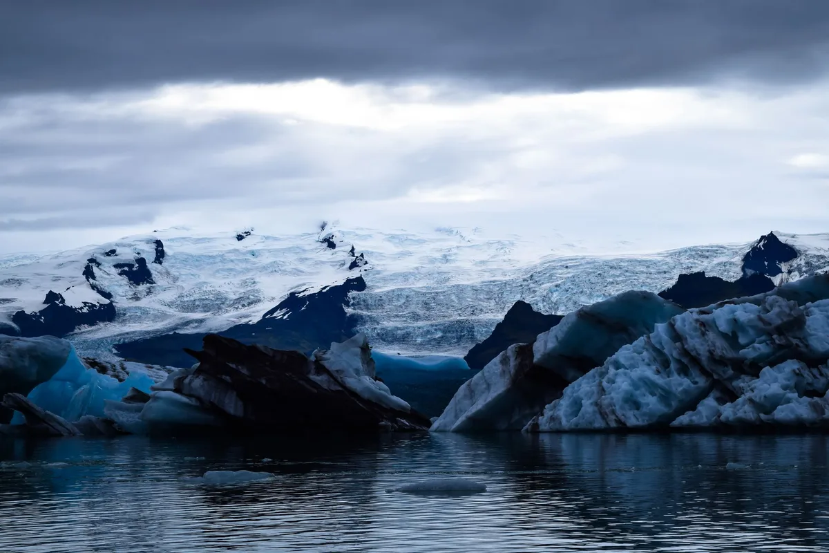 Iceberg diagram showing three distinct layers of the internet - surface web at the top in bright light, deep web in middle section partially submerged in shadow, dark web at the bottom in complete darkness, representing the structure and relative sizes of each layer.