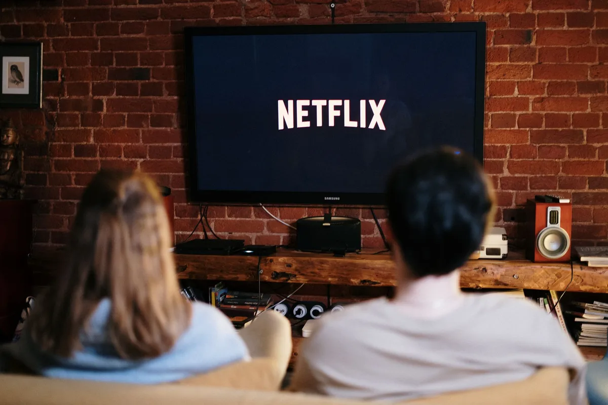 Mano sosteniendo un control remoto apuntando a una pantalla grande de televisor en una sala de estar moderna