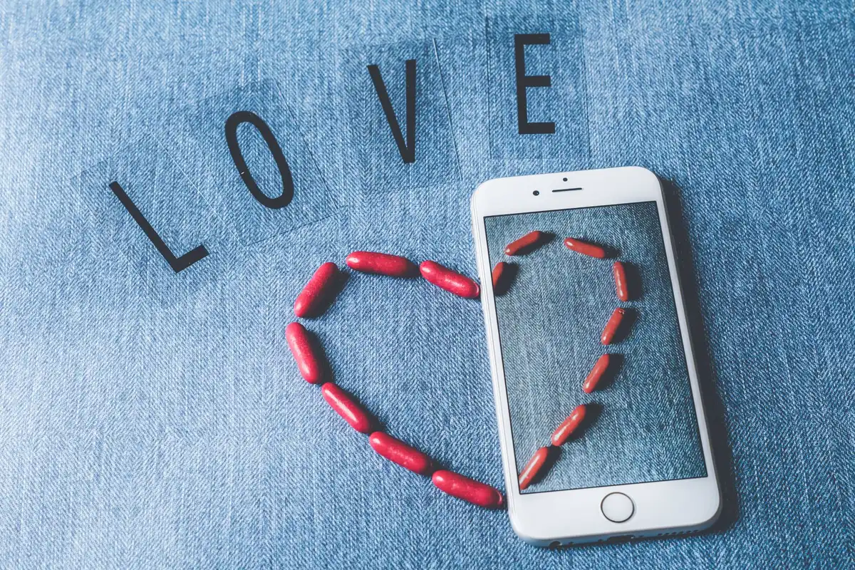 Smartphone screen displaying a glossy, heart-shaped device with reduced notch and sleek aluminum edges, rendered in Apple's signature minimalist style with soft lighting