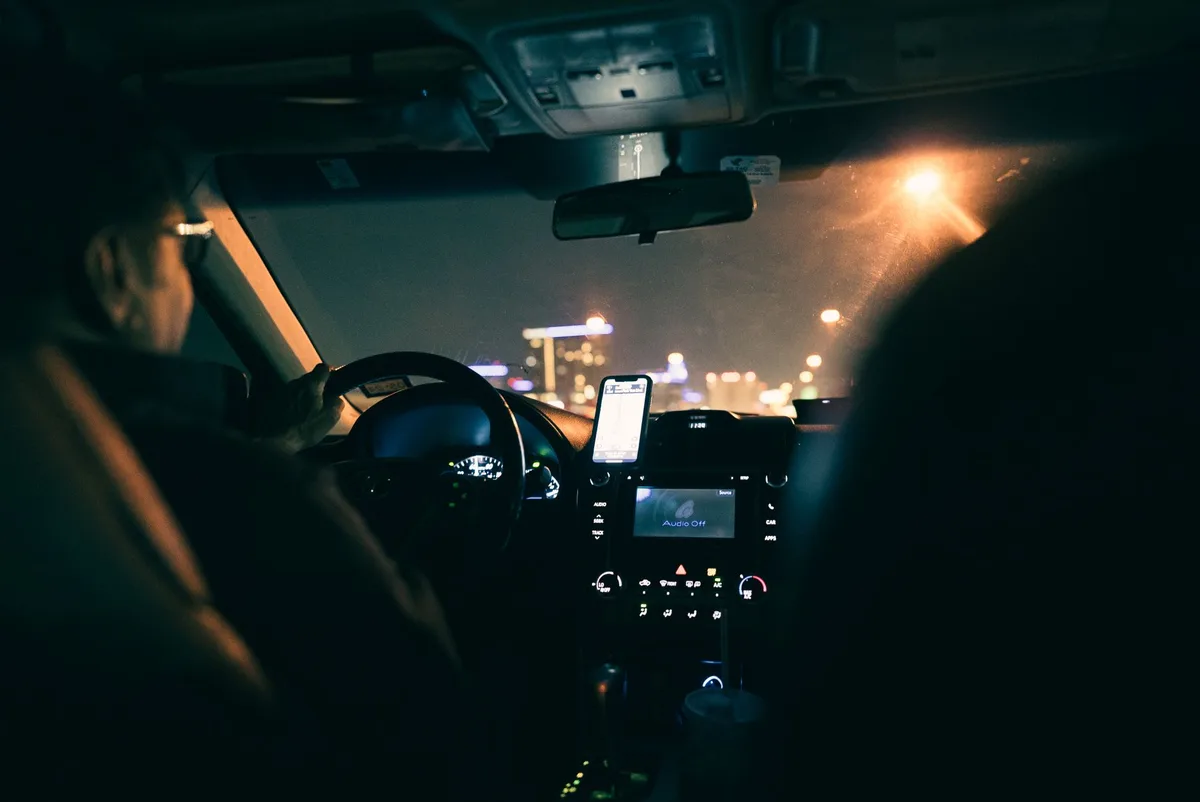 Smartphone displaying navigation app with radar warning icon on windshield, driver's perspective