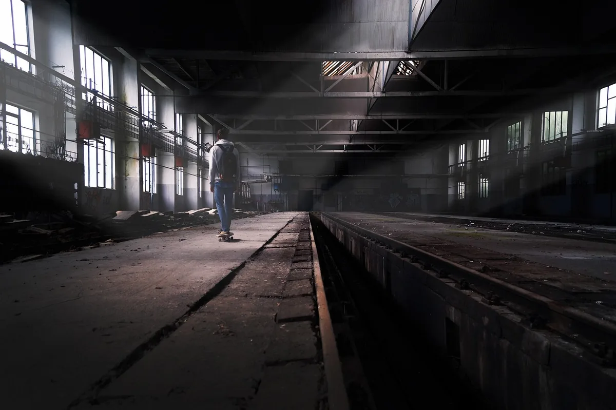 Túnel subterráneo oscuro con luz ultravioleta parpadeante iluminando objetos dispersos y siluetas en la distancia.