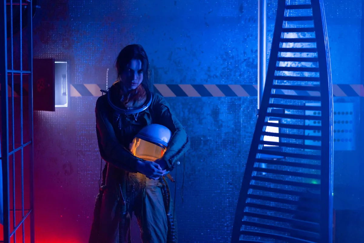 A dimly lit futuristic corridor with advanced technology lining the walls, a lone figure in power armor standing at a crossroads of branching passages, eerie blue and orange lighting creating tension and isolation.
