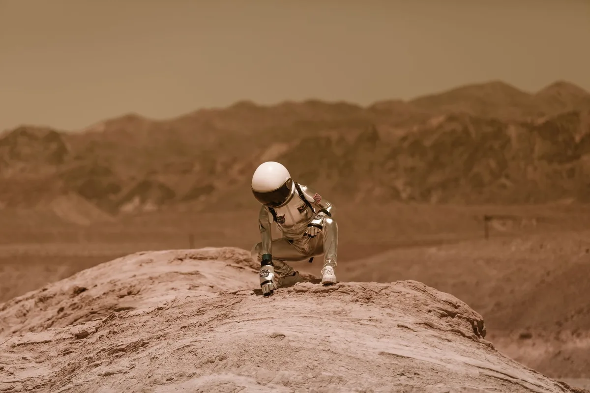 A sprawling alien landscape with towering structures and bioluminescent flora, a first-person view from inside a power suit helmet with HUD elements visible at the edges, golden and purple atmospheric lighting suggesting exploration of unknown worlds.