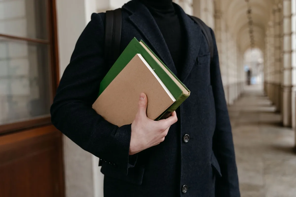 A student's backpack open with a tablet visible among books and school supplies, natural daylight on a desk