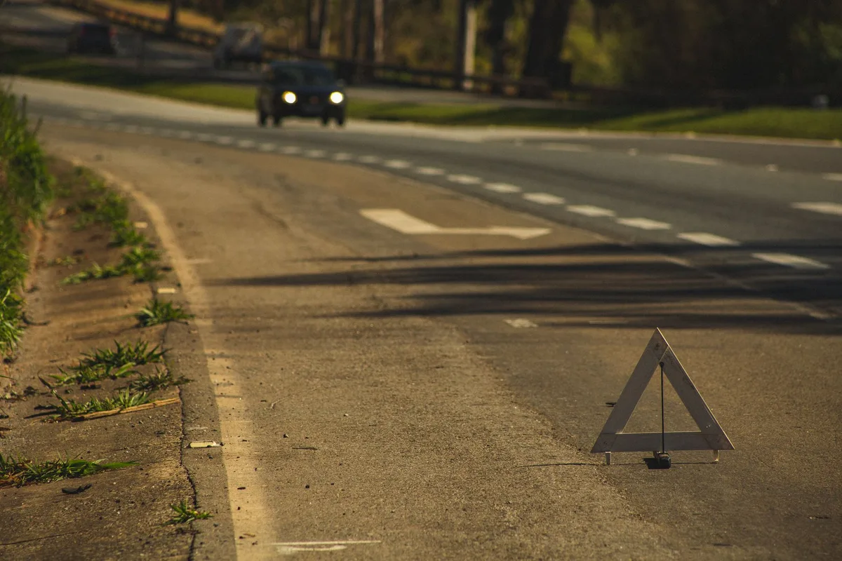 Triángulo de emergencia tradicional colocado en la carretera junto a un vehículo averiado