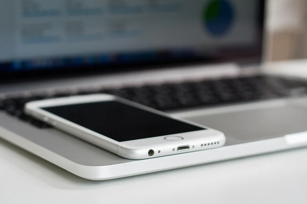 Empty workspace with an iPhone on a desk next to a notebook and pen, a faint screen glow suggesting a shortcut being generated