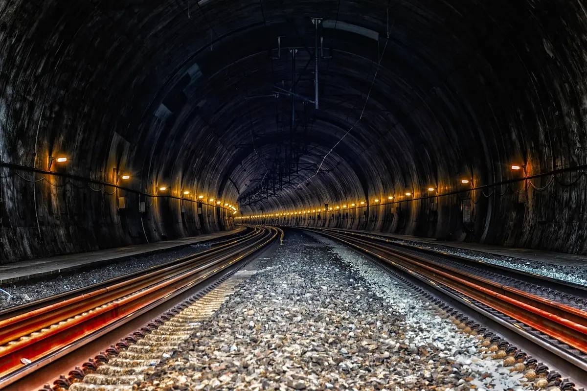 dim underground tunnel corridor with scattered lanterns and stone rails, distant light at the far end