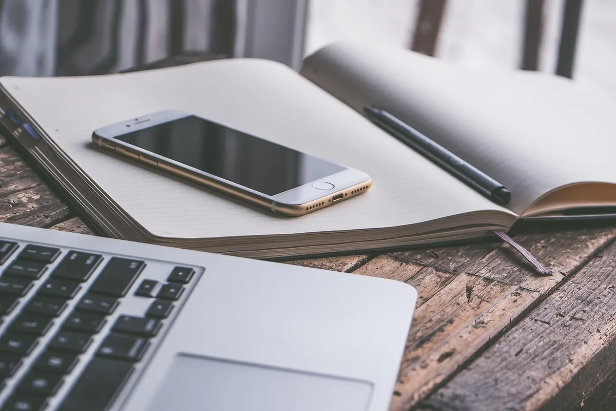 An empty smartphone resting on a neutral desk surface, battery icon on a printed spec sheet beside it, no logos or brand names visible