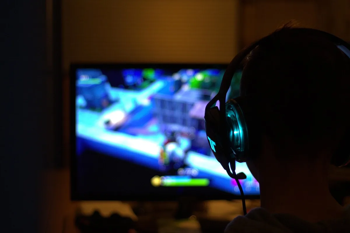 Controller held by anonymous gamer hands in professional gaming setup, neon-lit gaming room with multiple monitors, focused concentration on screen