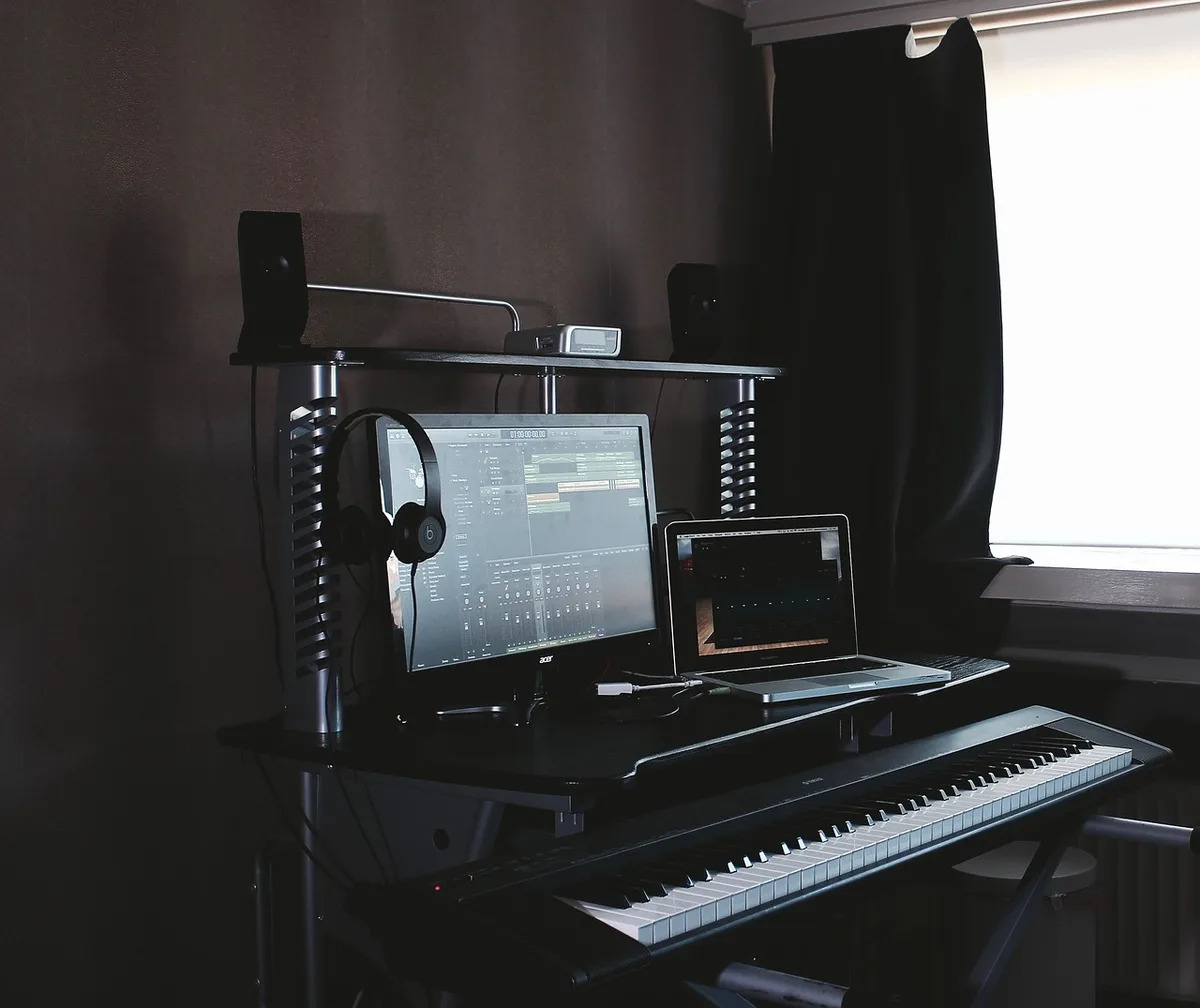 Two anonymous compact speakers on a desk flanking an unbranded laptop, cables hidden, subtle room plants in background