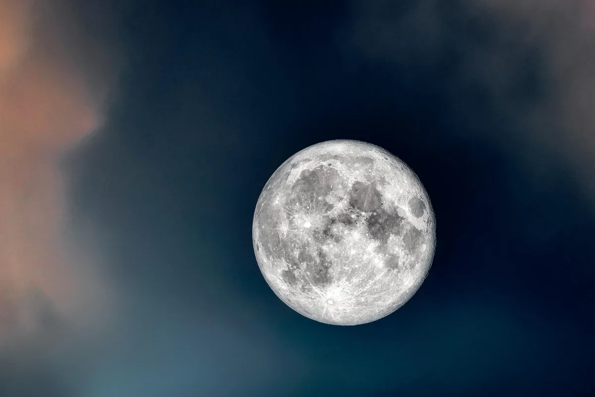 Campo oscuro con trípode y prismáticos apuntando al cielo nocturno y la Luna brillante