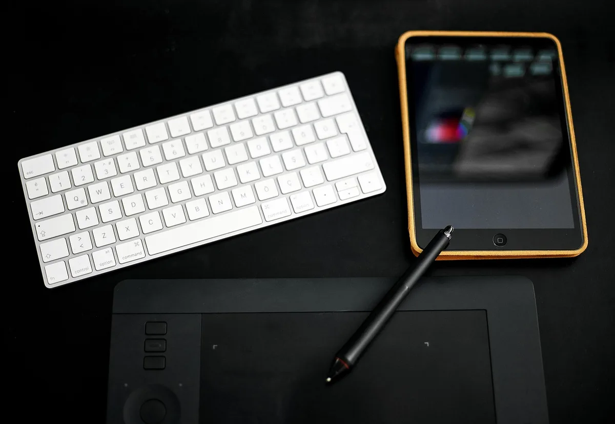 A minimal desktop scene with an unbranded thin keyboard next to a tablet on a simple stand, a compact notebook and a pen nearby, bright natural light — evokes productivity