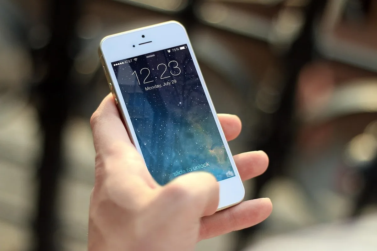 Anonymous hands holding a smartphone, a family photo projected on a TV screen in the background
