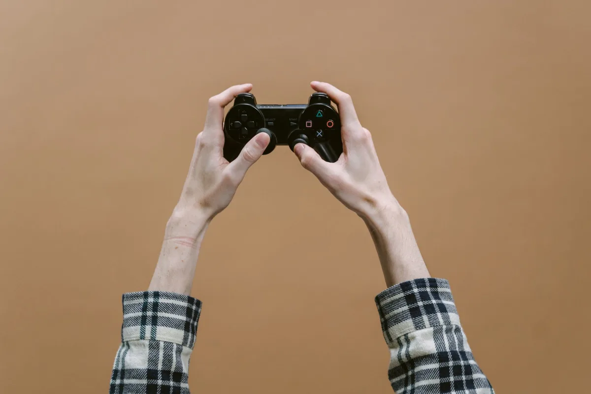 Close-up of anonymous hands holding a generic game controller in front of a bright screen showing lush blocky foliage and enhanced lighting; no faces, no branding
