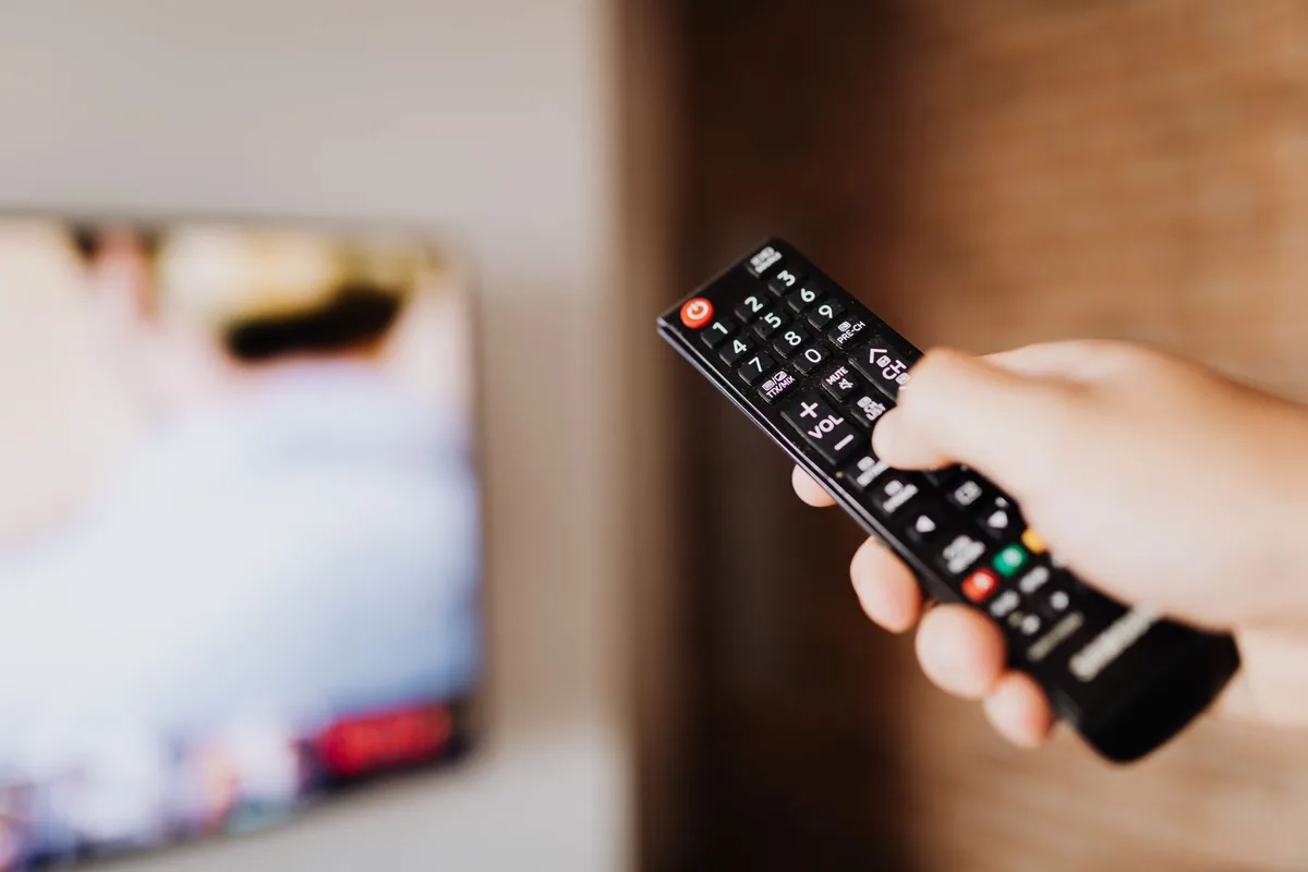 Close-up of an anonymous TV remote on a table beside a Halloween decoration, focus on the remote button and blurred screen in background
