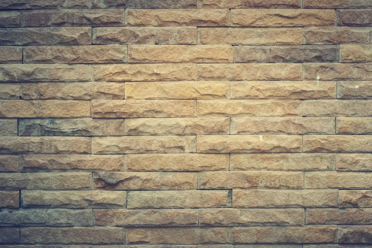 Close-up of an empty stone wall with four square and hexagonal recesses, scattered books and a broken glass display case nearby