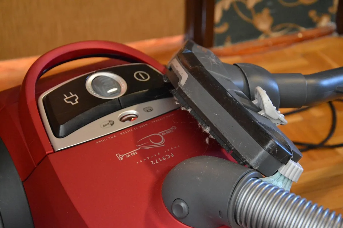 a clean unbranded cordless stick vacuum leaning against a neutral wall, folded low to show a slim profile and floor clearance