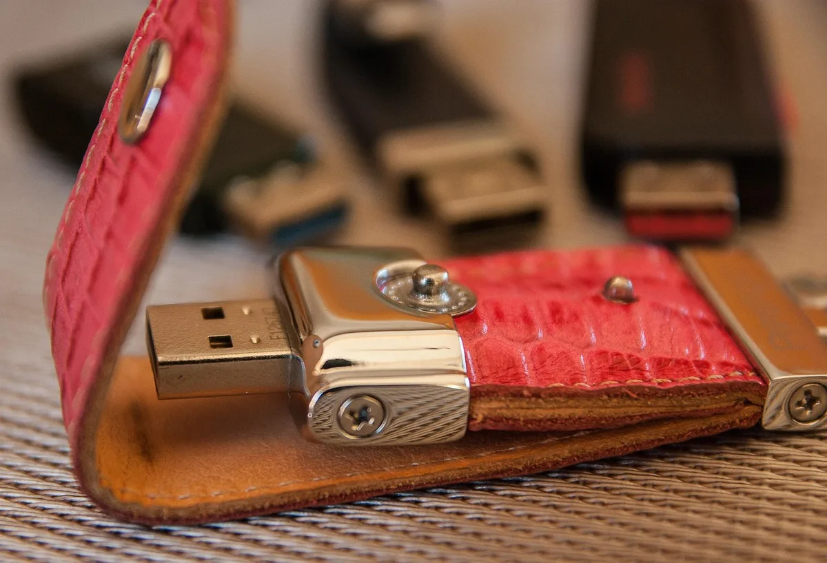 A compact USB stick and an unbranded laptop on a plain desk, an anonymous hand about to plug it in; focus on the USB and laptop port